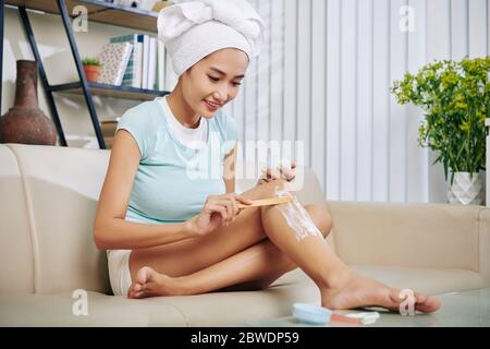 Positive young Asian woman applying hair removal cream after shower Stock Photo