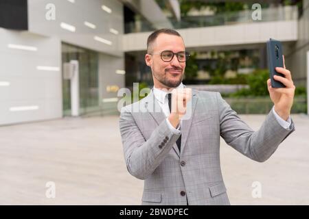 Handsome Hispanic bald bearded businessman taking selfie with eyeglasses in the city Stock Photo