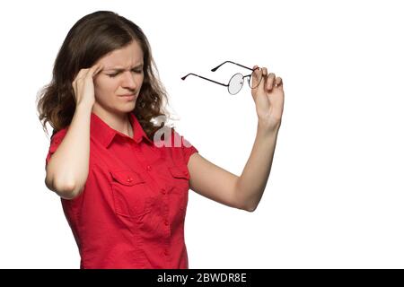 Beautiful young girl in a red shirt on a white background who has sore eyes and a head from glasses Stock Photo
