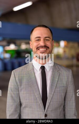 Happy Hispanic bald bearded businessman smiling at the sky train station Stock Photo