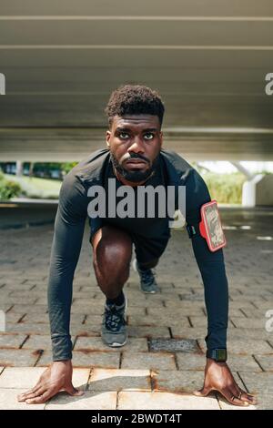 Serious young Black runner training for marathon and standing in start position ready to run Stock Photo