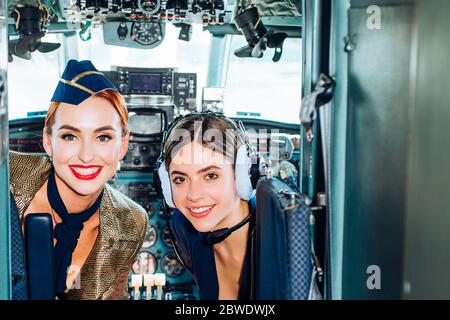 Woman pilot in aviation headsets. Pretty Stewardess. Portrait of attractive young woman pilot in cockpit. Portrait of young pilot in uniform posing Stock Photo