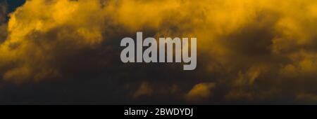 Panorama beautiful golden fluffy clouds illuminated by disappearing rays at sunset, thunderclouds floating across sunny blue sky to change season Stock Photo