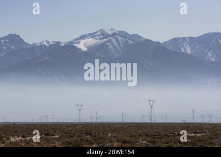 High voltage pylons on dry grassland in morning fog Stock Photo