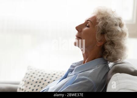 Peaceful old woman leaned on couch breathing fresh conditioned air Stock Photo