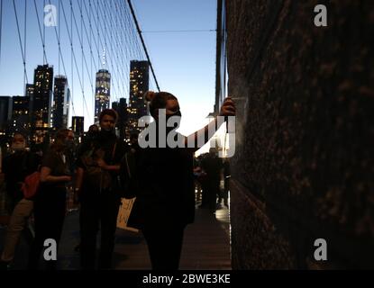 New York, United States. 01st June, 2020. A woman spray paints graffiti on the Brooklyn Bridge as protests around the country continue over the death of George Floyd at the hands of the Minneapolis police in New York City on Sunday, May 31, 2020. Former Minneapolis police officer Derek Chauvin was arrested Friday days after video circulated of him holding his knee to George Floyd's neck for more than eight minutes before Floyd died. All four officers involved in the incident also have been fired from the Minneapolis Police Department. Photo by John Angelillo/UPI Credit: UPI/Alamy Live News Stock Photo