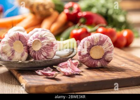 Five heads of garlic on a cutting board with various vegetables in the background Stock Photo