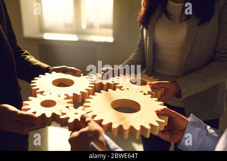 Business people holding wooden gears in their hands connect at a business meeting in the office. Stock Photo
