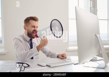 Angry displeased boss businessman shouting in megaphone into a computer Stock Photo