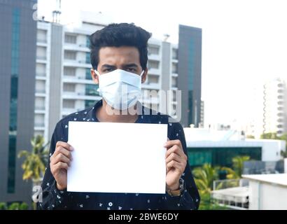 Man wearing medical mask and holding white blank paper with copy space, place for text image.selective focus on white paper. Stock Photo