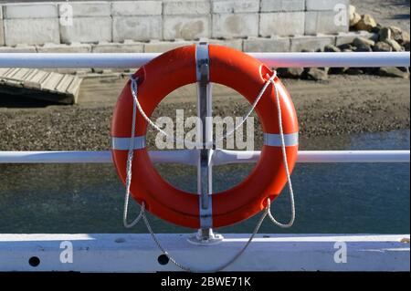 A safety precaution, an orange life ring is roped to rails on a pier by the sea Stock Photo