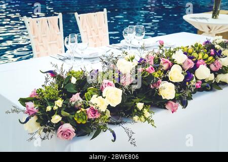 Newlyweds table at the wedding reception dinner decorated with flowers. Tropical location, resort wedding concept. Toned image with place for text Stock Photo