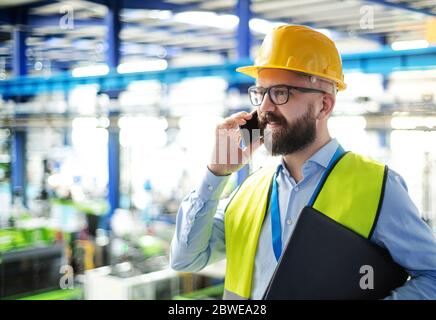 Technician or engineer with hard hat standing in industrial factory, using telephone. Stock Photo