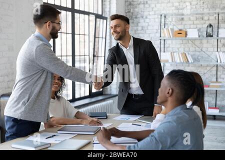 Smiling business partners shaking hands at group negotiations Stock Photo