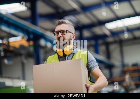 Man worker working in industrial factory or warehouse, carrying box. Stock Photo