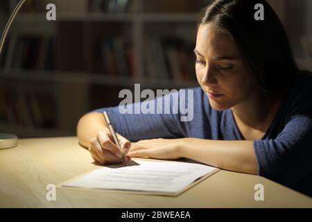 Serious woman signs contract at night in the living room at home Stock Photo