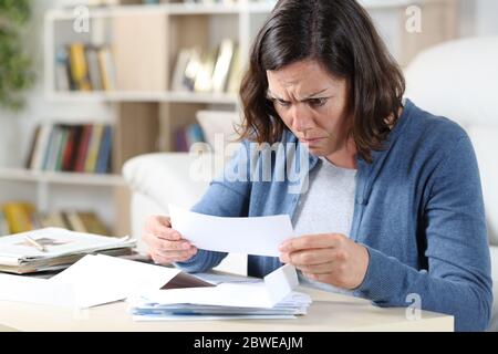 Confused adult woman looking at receipts sitting in the livingroom at home Stock Photo