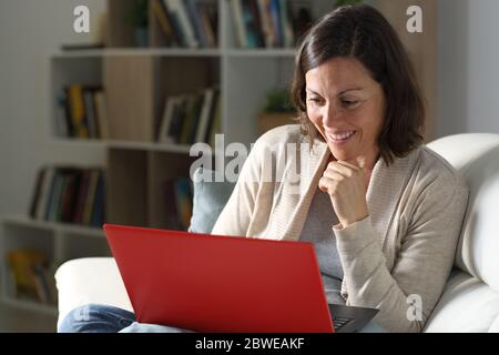 Happy adult lady streaming online content on laptop sitting on the sofa at night at home Stock Photo