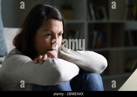 Pensive adult woman looking away thinking sitting on the floor in the livingroom at night at home Stock Photo