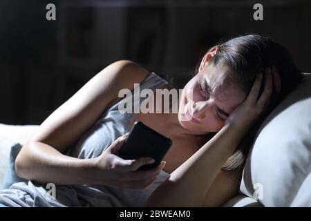 Sad woman complaining with smart phone sitting in the sofa at night at home Stock Photo