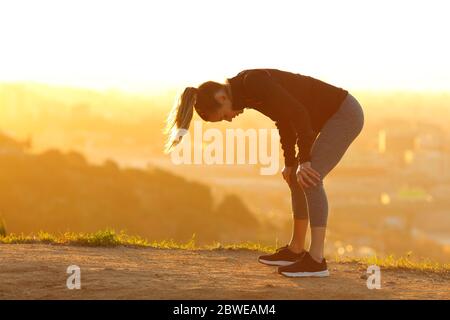 Side view portrait of a tired runner resting after exercise in city outskirts at sunset Stock Photo