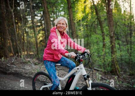 Active senior woman with e-bike cycling outdoors in nature. Stock Photo