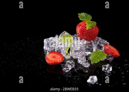 Strawberries, mint leaves and ice cubes on a black background with reflection Stock Photo