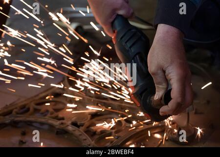 Front view of a man's hands working on a metal part of a garden bench, using an electric grinder while sparks are flying around in the industrial Stock Photo