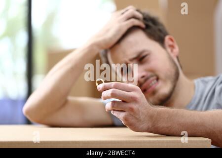 Sad husband complaining moving home after divorce and holding wedding ring surrounded by boxes Stock Photo