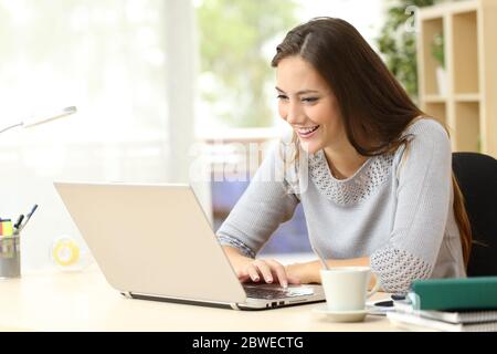Happy student woman reading content on a laptop sitting on a desk at home Stock Photo