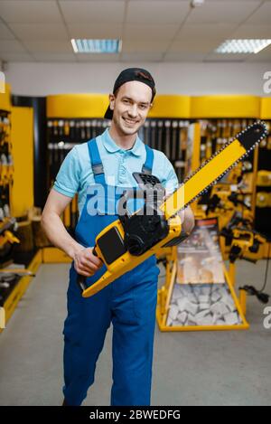 Male worker holds chainsaw in tool store Stock Photo