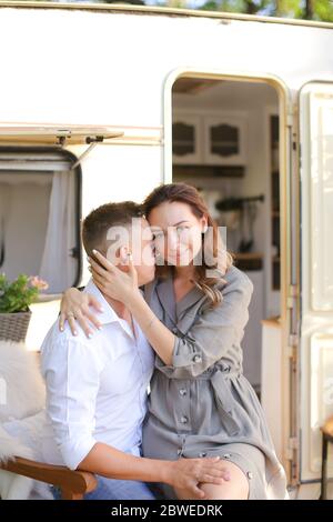 Portrait of young nice wife hugging husband near house on wheels. Stock Photo