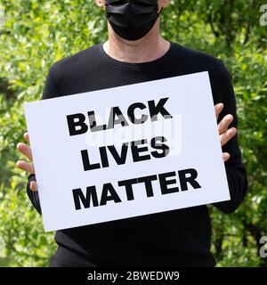 Man in medical black mask holds a white banner with the text BLACK LIVES MATTER. Protests erupt for a across the US over the death of George Floyd. Stock Photo