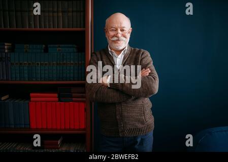 Cheerful elderly man in glasses poses at bookcase Stock Photo