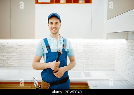 Plumber in uniform fixing faucet in the kitchen Stock Photo