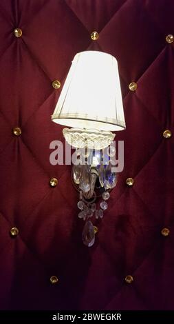 Retro bedroom lamp with a red wall. Antique sconces hanging on a wall of textile with buttons Stock Photo