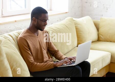 African man sitting on couch typing business letter on laptop Stock Photo