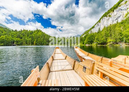 Beautiful view of traditional wooden rowing boat on scenic. Summer mountain lake pass scenic morning light at sunrise clouds over blue sky green trees Stock Photo