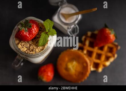 Homemade vegetarian breakfast, yogurt with strawberry and muesli on a dark background table top view. Stock Photo