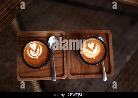 Two Cups of hot cappuccino on wooden desk with spoons on glass table background. Breakfast time. Top view. Stock Photo