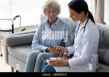 Physician manually takes blood pressure to elderly woman patient Stock Photo