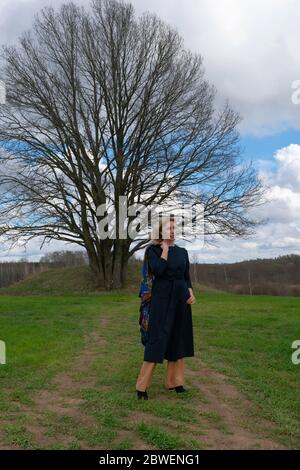 a blonde with long hair enjoys freedom, a middle-aged woman walks alone on a dirt road among green fields Stock Photo