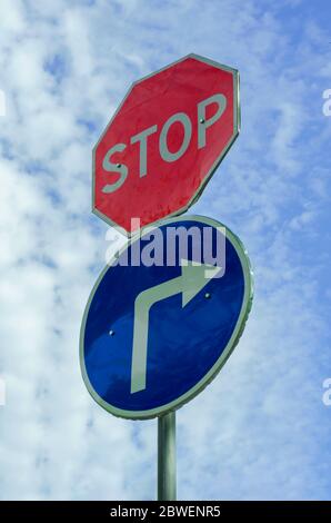 Road sign STOP and movement to the right on the background of the cloudy sky. Two road signs on one pillar. Ambiguous motivational background. Stock Photo