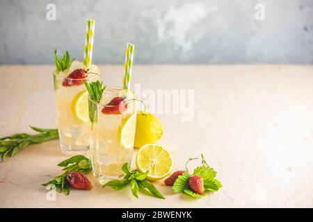 Two glasses of cold icy refreshing drink with lemon and strawberry served with bar tools on light pink table. Fresh cocktail drinks with ice fruit and Stock Photo