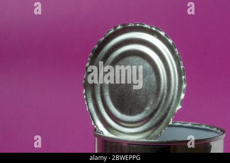 Open tin can lid close-up. Torn uneven edges of a metal cover on a purple background. Canned food. Place for text Stock Photo