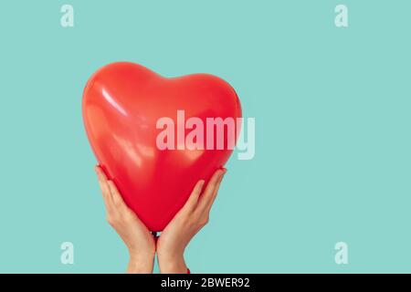 Woman is holding red heart shaped balloon to a turquoise wall background. Valentine day and romance concept Stock Photo