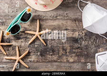 Sunglasses, starfish, summer hat and protective face mask on wooden background. Coronavirus summer concept.