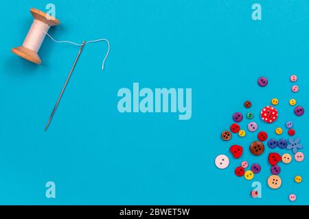 Multi-colored buttons are scattered on the table, a needle, a spool of thread. Accessories for sewing. Top view with copy space, flat lay. Stock Photo