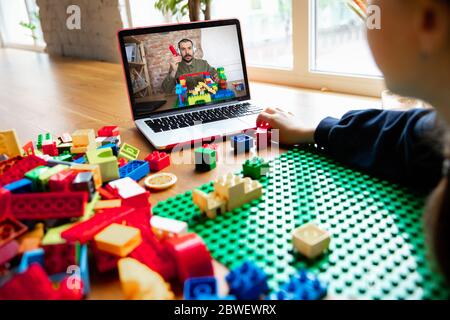 Girl playing with constructor at home, watching teacher's online tutorial on laptop. Digitalization, remote education concept. Technologies and devices. Man showing, giving online lesson. Artwork. Stock Photo