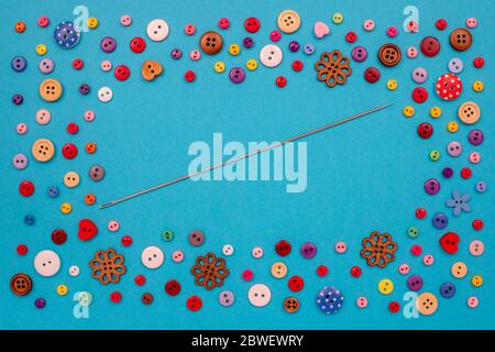 Multi-colored buttons are scattered on the table, a needle. Accessories for sewing. Top view with copy space, flat lay. Stock Photo